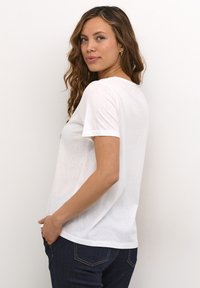 T-shirt bianco a maniche corte realizzato in tessuto leggero, con una vestibilità comoda e scollo rotondo, abbinato a jeans blu scuro.