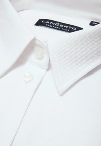 Biała koszulka polo z teksturowanym materiałem, dwa guziki przy kołnierzyku oraz metka z napisem "LANCERTO Comfort Plus."