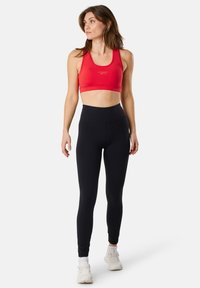 Reggiseno sportivo rosso con un design elegante, abbinato a leggings neri a vita alta. Entrambi gli articoli hanno una texture liscia e una vestibilità moderna.