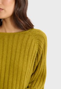 Sweter dzianinowy w oliwkowym kolorze z prążkowaną teksturą, szerokim dekoltem i opuszczonymi szwami ramion. Miękki, lekki materiał.