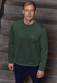 Grüner Pullover aus weichem Stoff, mit rundem Halsausschnitt und langen Ärmeln. Verfügt über ein kleines Logo auf der Brust und gerippte Bündchen.