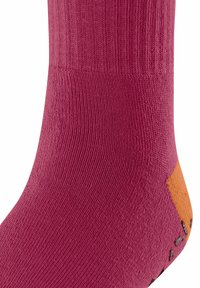 Zbliżenie różowej skarpetki z pomarańczową łatką na pięcie i teksturowanym splotem, ukazujące szczegóły i kontrast kolorów.