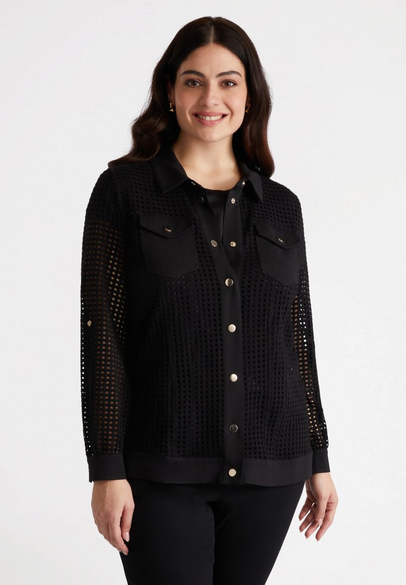 Blouse en mesh noir avec un devant boutonné, deux poches poitrine et un col et des poignets unis. Surface texturée avec un design moderne.