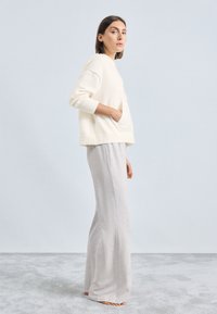 Light cream knitted sweater with long sleeves and a pocket, paired with light gray, loose-fitting, long sweatpants. Soft texture, casual fit.