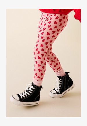 Ružové legíny s červenými srdcovými vzormi, skombinované s čiernymi vysokými teniskami s bielou podrážkou a ružovými rebrovanými členkovými ponožkami.