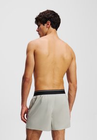 Hellgraue Badeshorts mit einem elastischen schwarzen Bund, die eine glatte Textur und einen lässigen Schnitt aufweisen, von hinten betrachtet.
