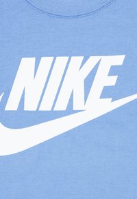 Μπλε βαμβακερό μπλουζάκι με μεγάλο λευκό λογότυπο «NIKE» και γραφικό σλόουσι στο μπροστινό μέρος. Στρογγυλή λαιμόκοψη και απαλή υφή.