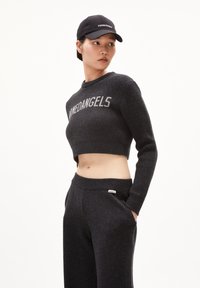 Suéter negro corto con texto gris "MEDANGELS," combinado con pantalones de chándal oscuros. Textura de punto suave y ajuste relajado. Gorro con el logo "PERMANENT".