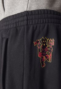 Mustat collegehousut, joissa monivärinen graafinen logo vasemmassa taskualueessa. Vyötärönauha on joustinneulosta mukavuutta varten.