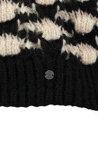 Schwarzer Strickstoff mit beigefarbenem Gewebe-Muster und kleinem runden silbernen Anhänger, der an der gerippten Kante befestigt ist.