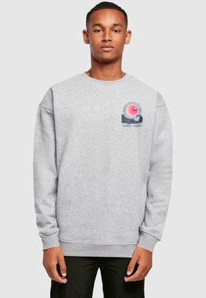 Grå sweatshirt med rund hals, der har et farverigt solnedgangsdesign og bølger på venstre side. Lange ærmer og ribbede manchetter.