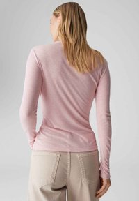 Rosa Langarmshirt aus weichem, leichtem Stoff mit Rundhalsausschnitt und tailliertem Design, kombiniert mit beigen, hoch taillierten Hosen.