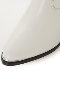 Zapato blanco de cuero de punta afilada con un diseño elegante. Presenta un acento plateado en la punta y una suela negra para contraste. Textura suave.