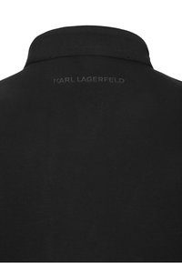 Musta poolkaotune paita, millel on lame krae, valmistatud siledast kangast, tagaküljel embosseeritud tekst "KARL LAGERFELD".