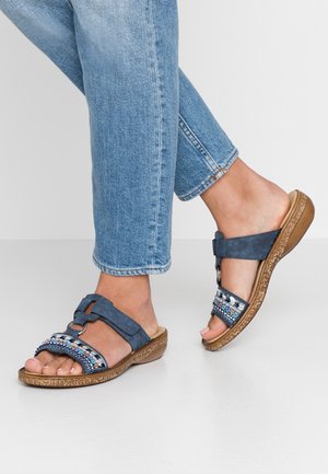 Blue suede sandals with decorative beading, a wide strap, and a slight wedge sole, paired with light blue cuffed jeans.