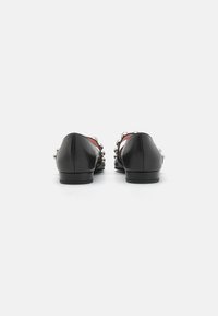 Black leather flats with a low heel, featuring silver-tone embellishments along the sides and a smooth texture. Red interior accents.