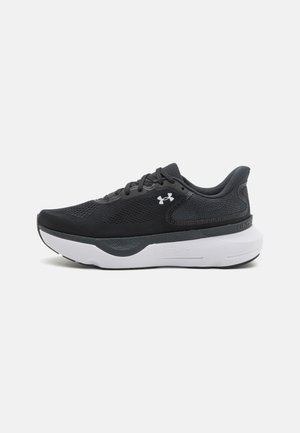 Chaussure de sport noire avec une tige en mesh respirant, des accents réfléchissants et une semelle de confort blanche. Elle est dotée de lacets et de détails de marque.