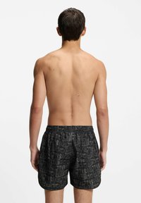 Musta uimapuku, jossa on joustava vyötärö, varustettuna toistuvalla logo-kuvioinnilla. Kevyt, nopeasti kuivuva materiaali. Yksinkertainen takanäkymä.