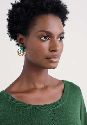 Suéter verde tejido con un cuello amplio, con detalles texturizados. Pendientes circulares con acabado metálico dorado y detalle en color azul verdoso.