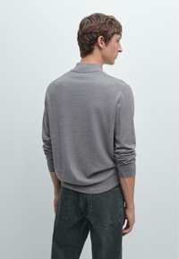 Grå stickad tröja med krage, åtsittande ärmar och ribbade muddar, tillsammans med mörkblå jeans. Strukturerad yta och avslappnad design.