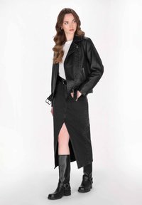 Giacca da moto in pelle nera con dettagli con borchie, t-shirt bianca, gonna in denim nera con spacco davanti e stivali neri fino al ginocchio.