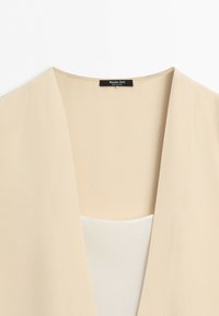 Close-up of beige blazer collar showing inner label with brand name Massimo Dutti and "Made in China" text.