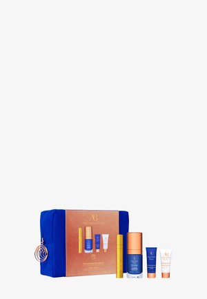 Trousse cosmétique bleue avec quatre produits de soin de la peau dans des tubes et flacons bleus, dorés et blancs, étiquetés Augustinus Bader, exposée à côté de la boîte d'emballage.