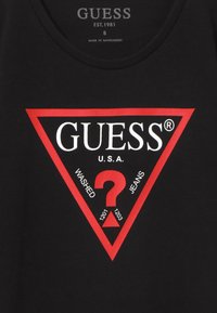 Musta paita, jossa on punainen kolmio-logo, jossa on valkoista tekstiä "GUESS U.S.A." ja lauseita "WASHED JEANS" punaisen kysymysmerkin ympärillä.