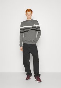 Suéter gris con rayas horizontales en negro, blanco y gris, combinado con pantalones negros y zapatillas burdeos, con un escote redondo y mangas largas.