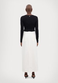 Zwarte top met lange mouwen en een aansluitend design, gecombineerd met een witte hoogsluitende denim rok. Makkelijk stof met zakken aan de achterkant.
