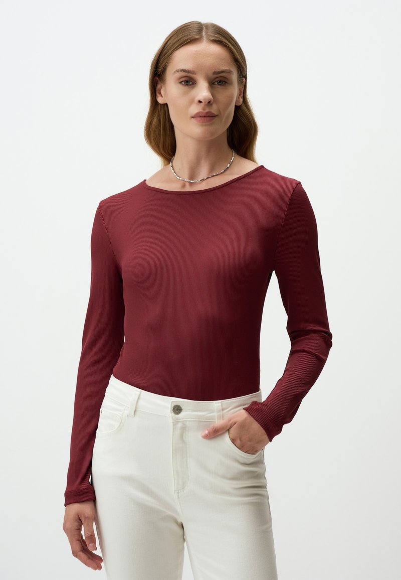 Langsleeve burgundy geribbelde top met ronde hals, gedragen met witte high-waisted broek. De top heeft een strakke pasvorm en een gladde textuur.