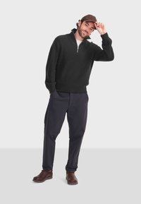 Czarna teksturowana bluza na zamek, ciemne spodnie i brązowe buty na slip-on. Ubranie charakteryzuje się swobodnym stylem i luźnym krojem.