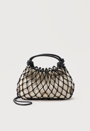 Sac à main en tissu beige enveloppé d'un filet noir noué avec une poignée noire structurée et une fine bandoulière amovible, posé sur un fond uni.