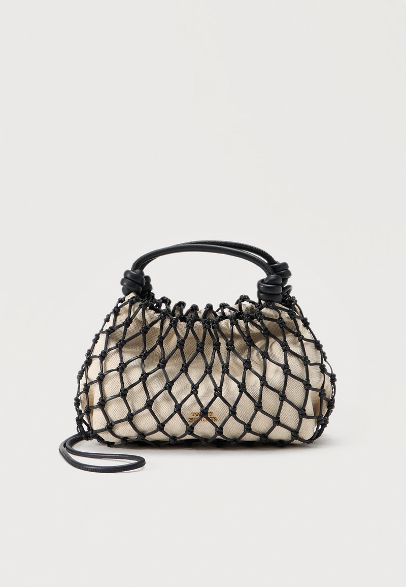 Μπεζ υφασμάτινη τσάντα χειρός, περιτυλιγμένη σε μαύρο διπλωμένο δίχτυ με σταθερό μαύρο χερούλι και λεπτό αποσπώμενο ιμάντα ώμου, τοποθετημένη σε απλό φόντο.