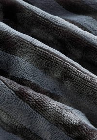 Mäkká, štruktúrovaná tkanina v odtieňoch šedej a čiernej, prezentovaná v jemných vlnách, zvýrazňujúca jej nadýchaný a útulný vzhľad.