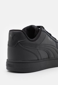Baskets en cuir noir avec col rembourré, surface texturée et logo Puma bien visible sur le talon. Elles présentent des coutures contrastantes et une semelle en caoutchouc.