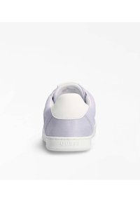 Fialová sneakers s hladkým povrchem, bílými koženými akcenty a gumovou podrážkou. Název značky vyražený na patě bílé podrážky.