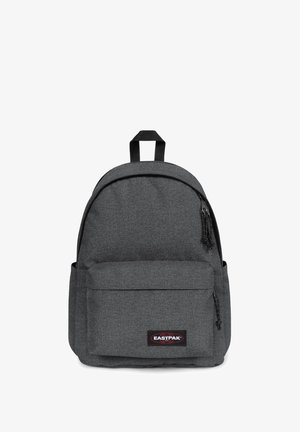 Mochila de tela gris con un diseño de parte superior redondeada, bolsillo frontal, correas ajustables dobles y un parche de logo negro. Presenta una superficie texturizada y detalles con cremallera.