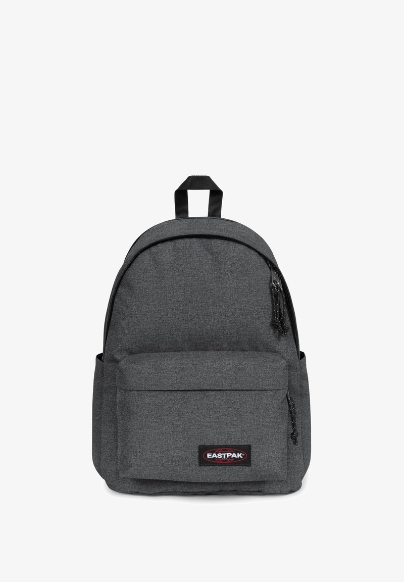 Šedý látkový batoh s kulatou horní částí, přední kapsou, dvojitými nastavitelnými popruhy a černou nášivkou s logem. Má texturovaný povrch a detail se zipem.