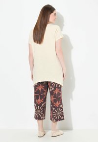 Lichtbeige kortärmige top met een gebogen zoom, gecombineerd met donkere cropped broeken met een patroon van palmen en geometrische ontwerpen. Beige instapschoenen.