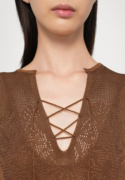 Bruine gebreide top met een V-halsontwerp en kruislings detail. De textuur is intricate met een patroonafwerking en zichtbare stiksels.