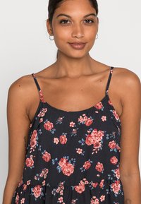 Vestido floral com fundo azul-marinho e rosas vermelhas e rosas. Feito de um tecido suave, com alças finas e uma silhueta fluida.