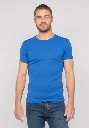 T-shirt en coton bleu à manches courtes et col rond. Présente un logo discret sur la poitrine. Associé à un jean en denim.