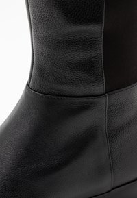 Bota de cuero negra con un acabado texturizado, panel de tela mate en contraste y bordes lisos para una silueta elegante.