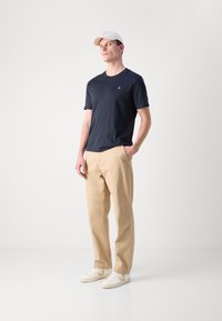 Marineblå T-shirt med korte ærmer og et lille logo, parret med beige bukser og hvide sneakers med et karakteristisk logo på siden.