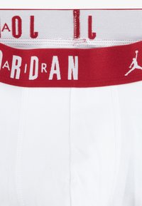 Biancheria intima bianca con elastico rosso in vita. L'elastico presenta la scritta "JORDAN" in caratteri bianchi e una silhouette del logo, evidenziando un design sportivo.