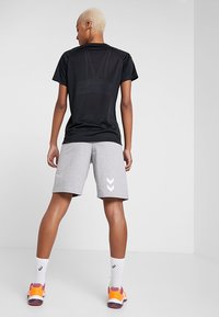 Svart sport t-shirt med korta ärmar och en grå logotyp, kombinerad med grå shorts med vit chevrontryck, bärs med färgglada sneakers.