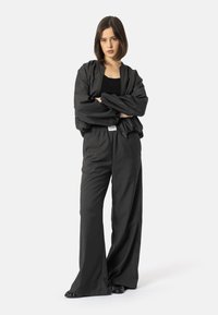 Černá bomber bunda přes černé tílko, doplněná volnými černými kalhotami. Tkanina je hladká, s uvolněným střihem a elastickými manžetami.
