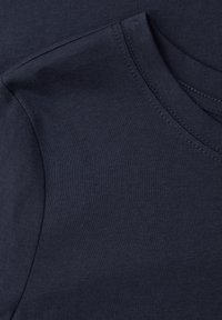 Gros plan sur l'épaule et l'encolure d'un t-shirt en coton bleu marine avec des coutures visibles et une texture lisse.