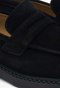 Zwarte suède loafers hebben een gladde afwerking, een band over de wreef en een rubberen zool met textuur en gestikte details.